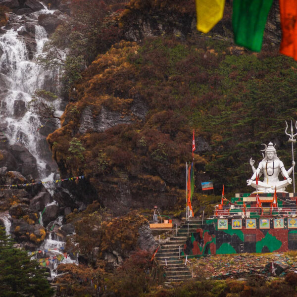 A statue of loard shiva sitting in front of a water fall.